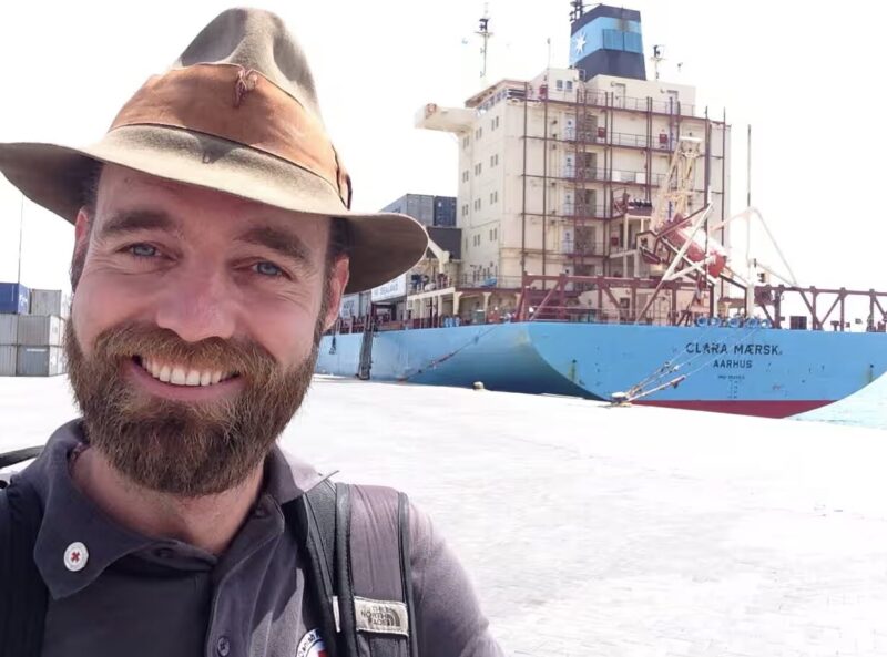 bearded man smiling in front of ship