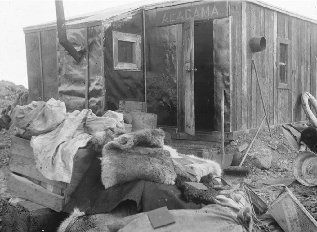 A ramshackle cottage with supplies strewn in front.