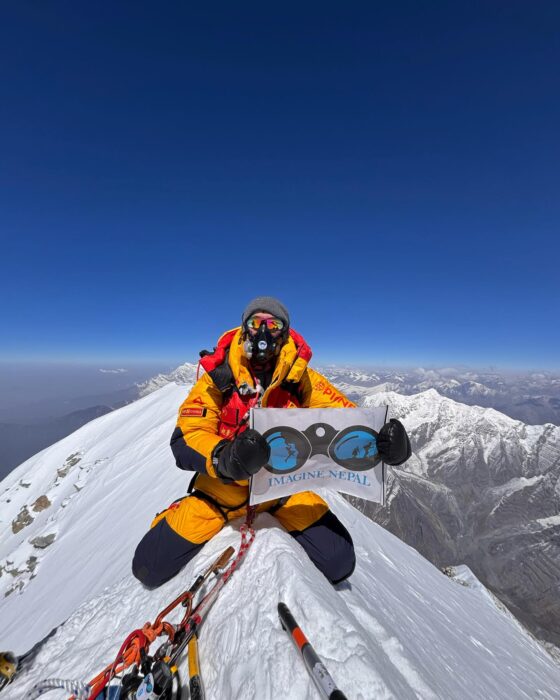 A climber on oxygen sits on top of the sharp snow ridge marking the summit of Annapurna. 