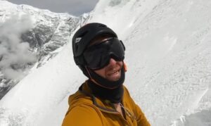 Close shot of a climber with helmet and dark glasses while standing on a steep snow slope.
