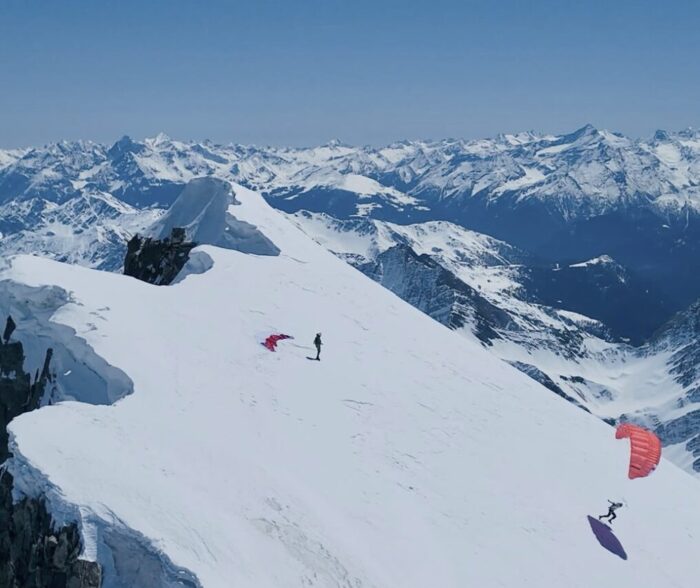 Two climbers taking off on paraglides from a snowy summit of Grandes Jorasses, Alps. 