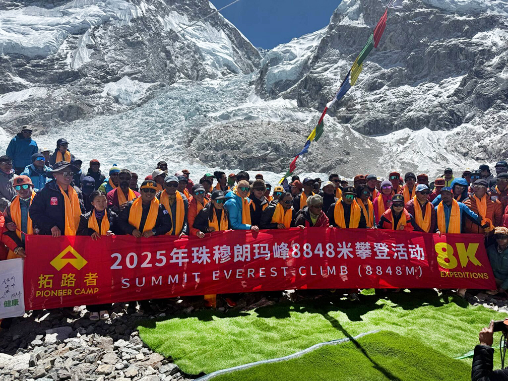 a huge group of climbers posing with a banner at Everest base Camp.