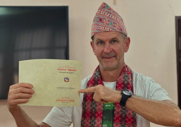 Climber with a khata scarf and a Nepalese hat holds a climbing permit for Everest.
