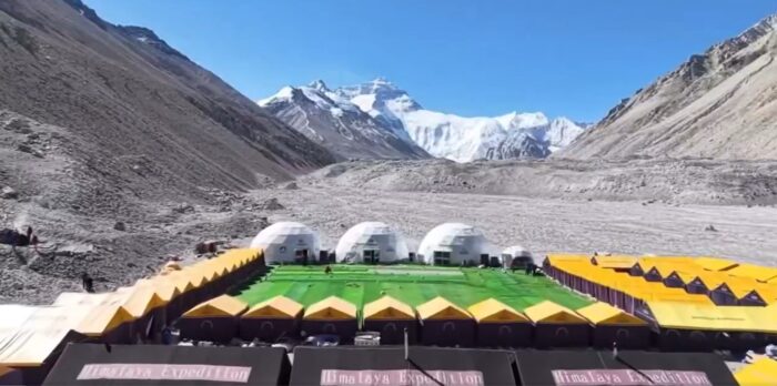 tents around an arrtificial grass field on the Tibetan plain, Everest in the distance.