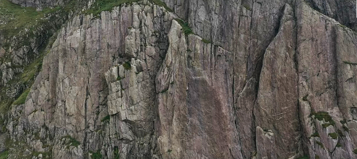 a small figure against a grey-brown cliff face