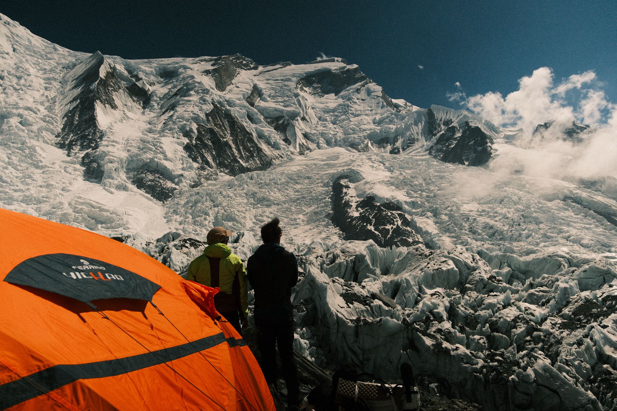Two climbers look up to Annapurna summit as they stand in front of an orange tent.