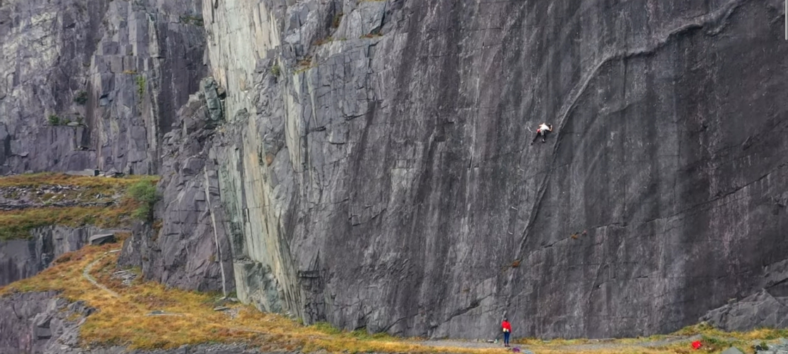 A small figure climbing a grey cliff.