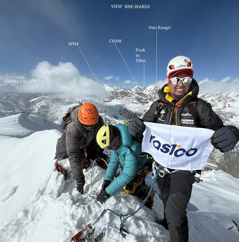 Climbers on a snowy summit, with some peaks in background.