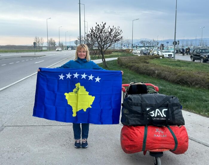 Uta Ibrahimi holds a big flag with Kosovo map, by a bicycle. 