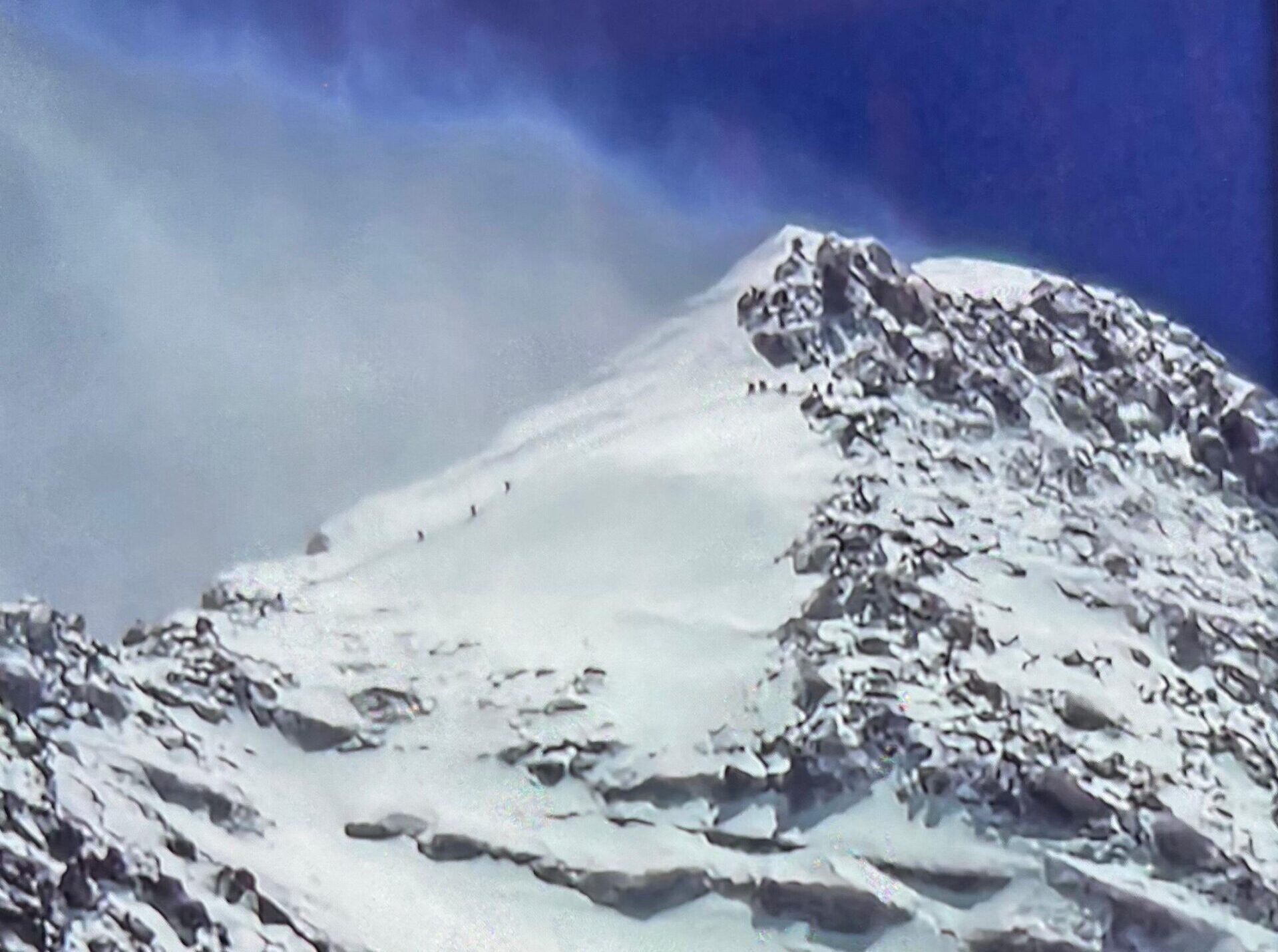 A tiny line of climbers up a snow slope on the pyramidal summit of Everest.