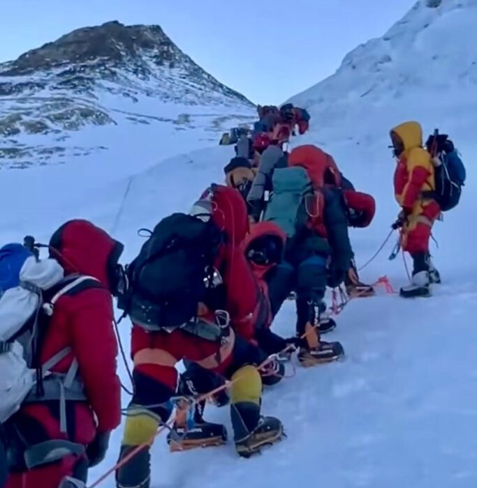 climbers in line on a fixed rope heading towards the summit area of Everest, seen in background. 