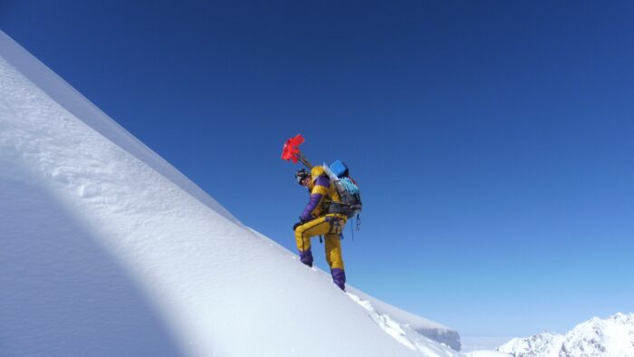 CLimber on a snow slope, carrying bamboo poles in the backpack. 