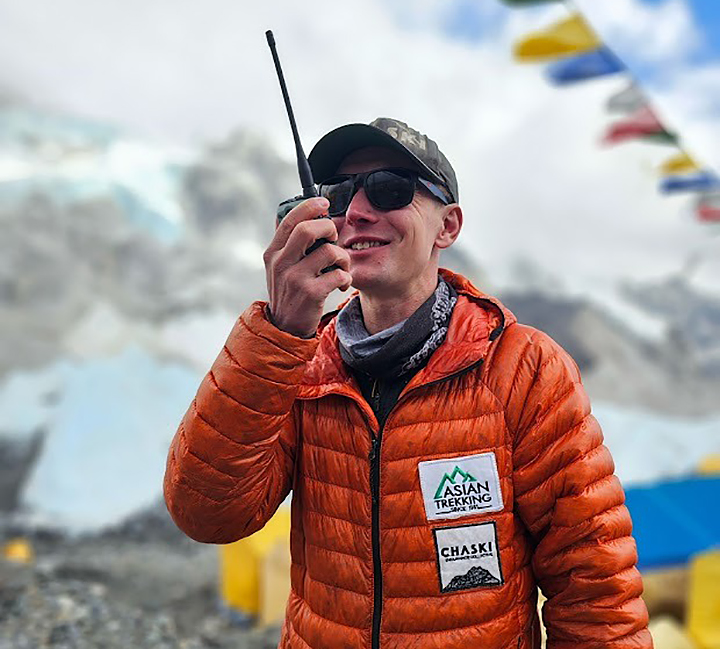 Tyler Andrews in a orange down jacket holding a walkie-talkie.