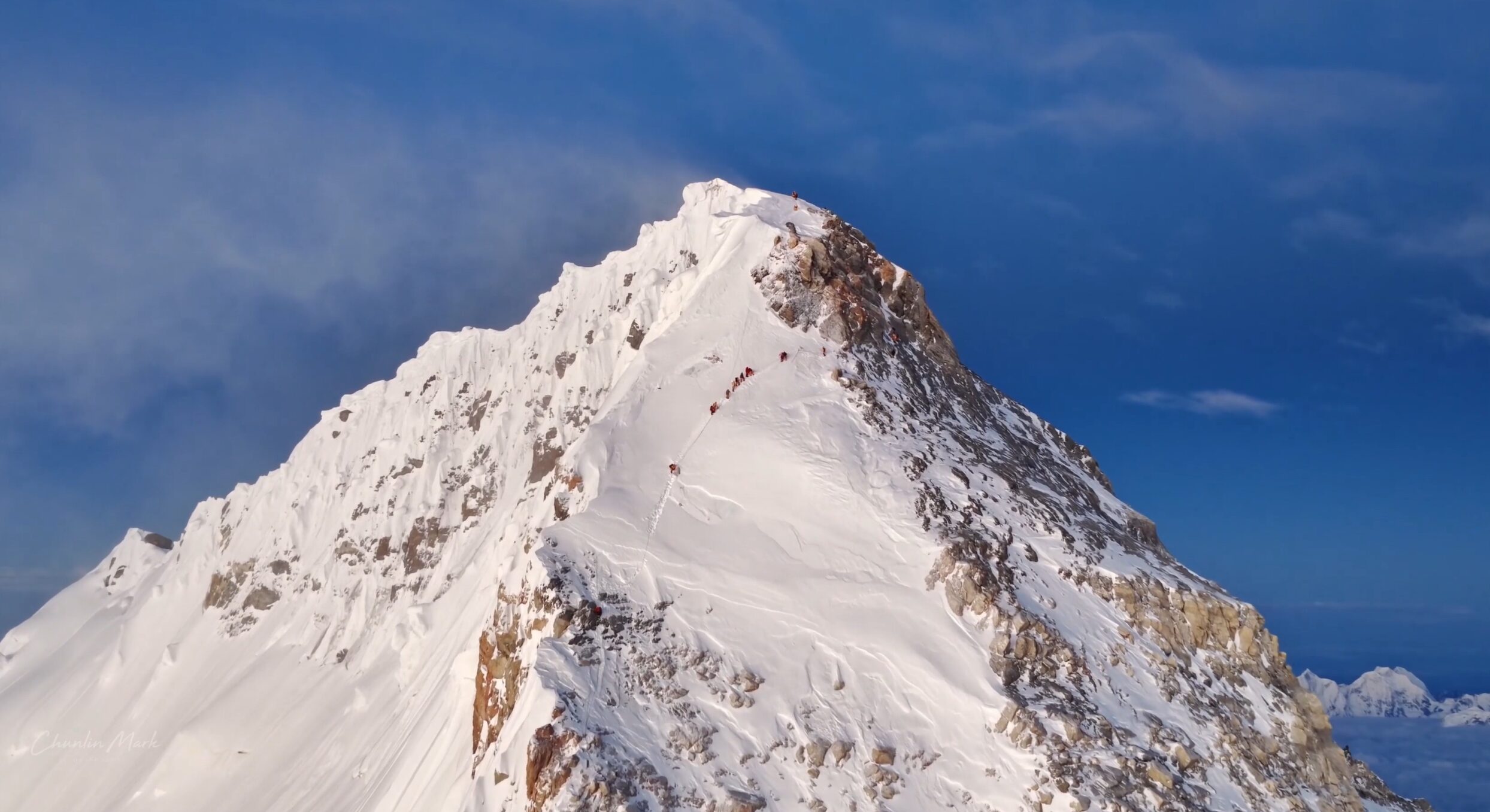 A small group of climbers in line, looking tiny on the final ramp leading to the summit of Everest, from Tibet.