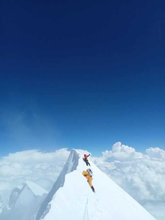 Climbers on a spiked snow summit rising above the clouds. 