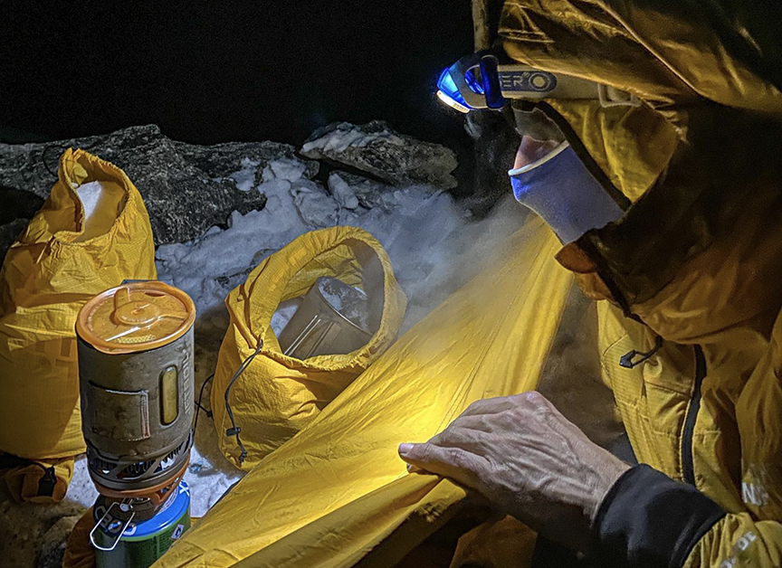 David Goettler with face covered and headlamp on, peers out if his tent in the night to cook in the night.