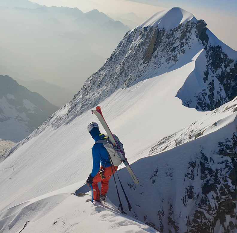 Alpinist with skis on his back, on a sharp snow ridge on Mont Blanc.