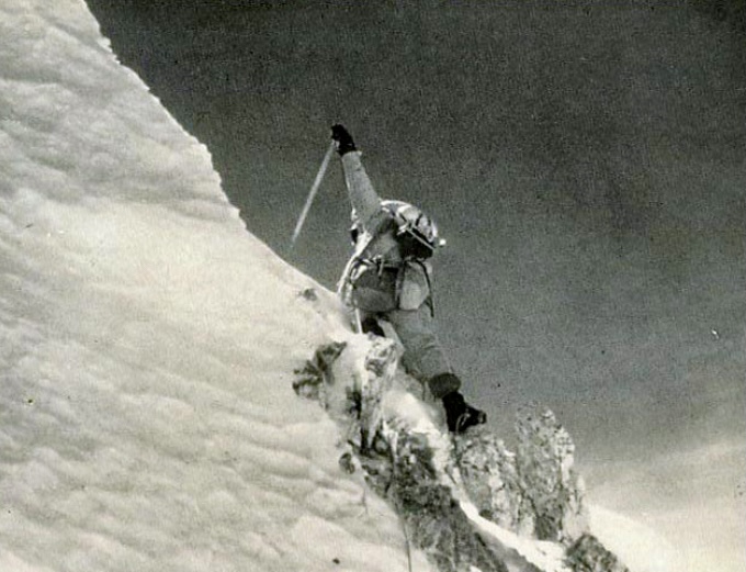 B&W image of a climber rising his ice axe under a snowy summit peak. 