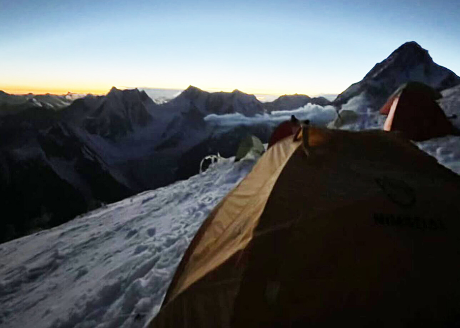 A tent on a snow slope with mountains in background at dawn/dusk