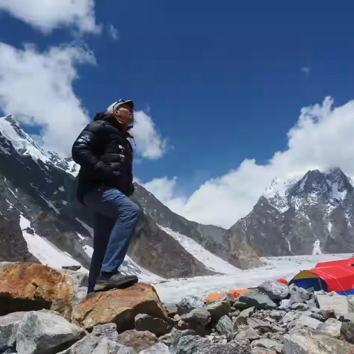 Climber with jeans and dawn jacket looks up from Broad Peak Base Camp. 