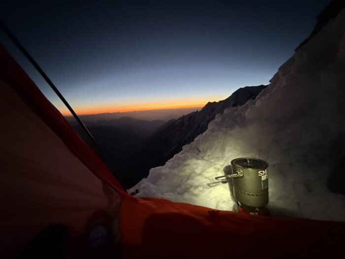 a pot on a stove in front of atent, and the sunset in background. 