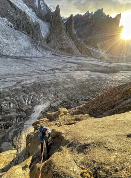 A climber ona granite face at sunset, a glacier at his feet. 
