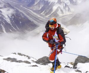 Climber in bright red and white clipped to a fixed rope on mised terrain on K2.