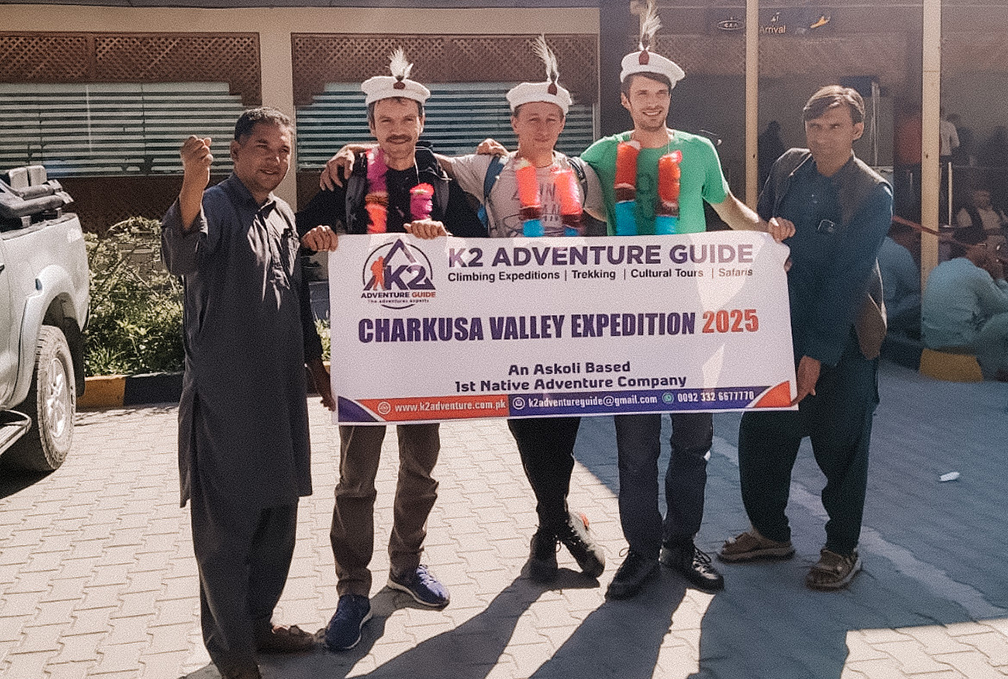 Three Polish climbers with local agents holding an expedition banner and weather local hats.