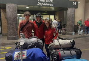 Climbers pose in front of the departures lounge of an airport with their duffel bags.