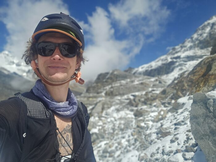 Selfie by Tyler Andrews with a rocky-snow slope behind. 