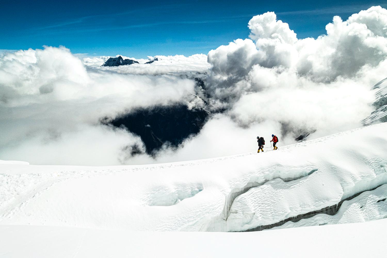 Two climbers on the summit ridge of Manaslu, clouds behind.