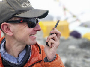 Close shot of Tyler Andrews at a rocky base camp, with an InReach device in his hand.