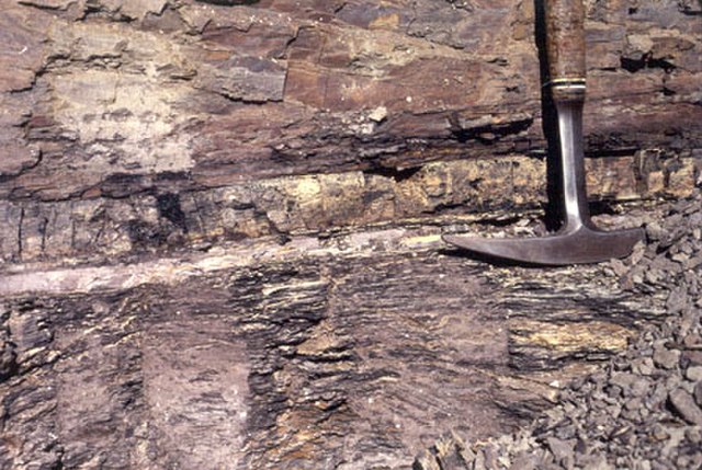 A striated rock face with a pick indicating a paler layer