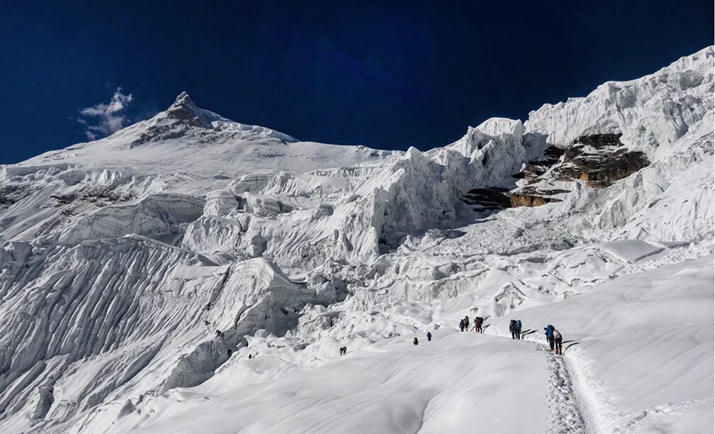 Climbers follow a well marked trail across and up Manaslu, toward the summit seen on the top left corner of the image.