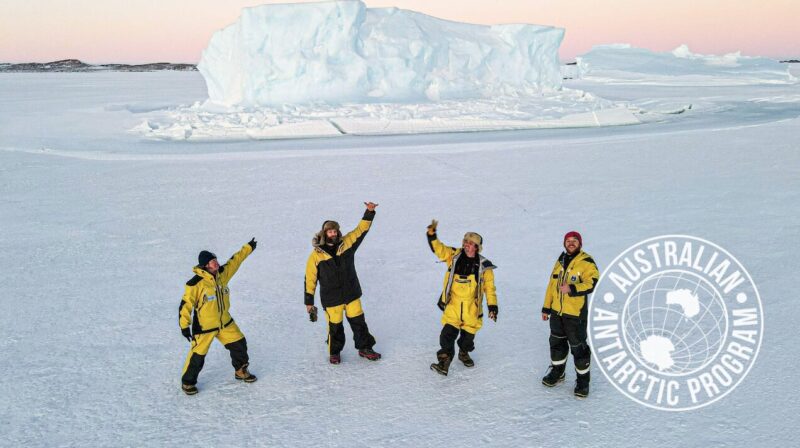 four people standing in a snowy environment, iceberg behind