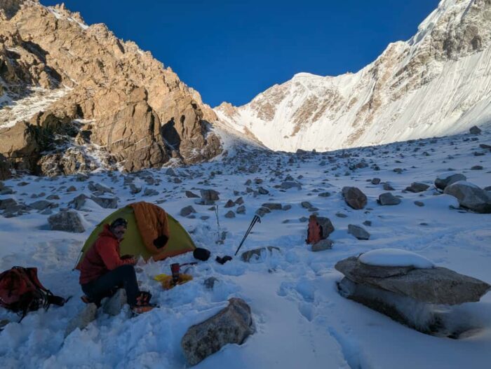A climber in front of a tent pitched on mixed terrain. 