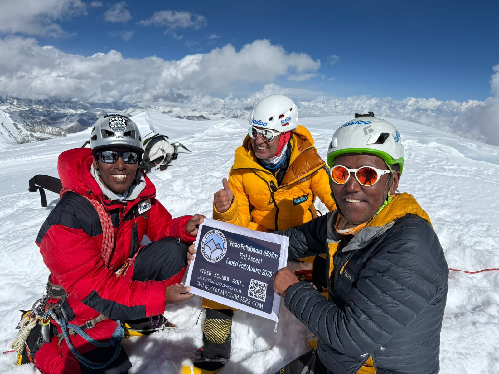 three climbers squat on a snowy summit.