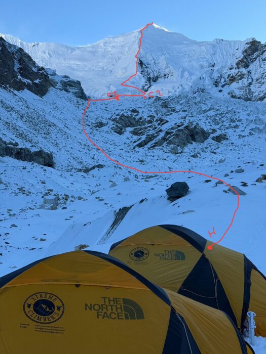 Tents in front of a snowy peak, with a climbing route marked in red. 