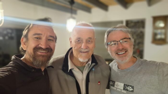 The three men smile in an indoor setting.