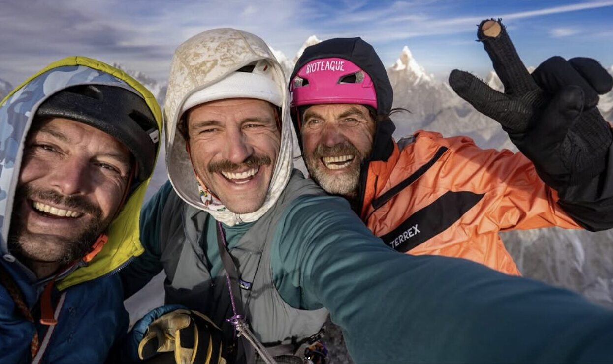 Three smiling climbers take a selfy on a summit.