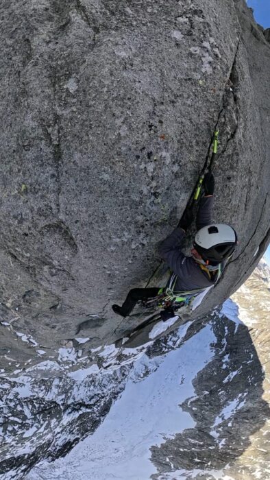 A climber on a slightly overhanging granite section up a crack on mixed conditions. 