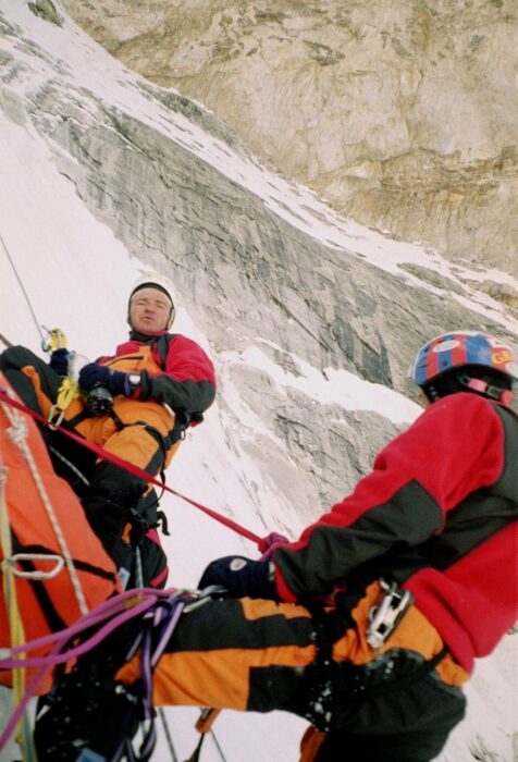 Two climbers belayed next to a portaledge in a mixed terrain face.