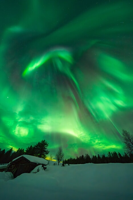 The Aurora Borealis dancing over a snow covered cabin in Finland