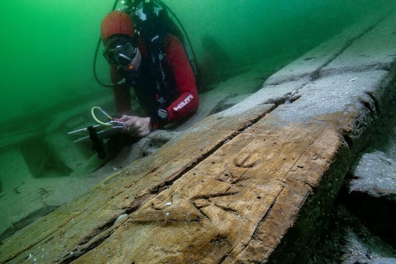 A scuba diver looks the Greek graffiti etched into the boat