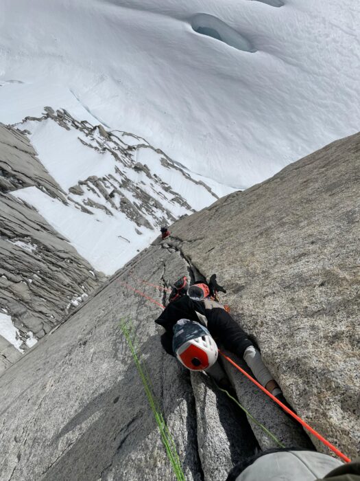 A climber up a vertical crack on a granite face, snow at his feet.