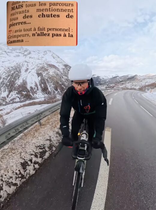 Dubouloz cyclinb on a road in bad weather, and a signal at the foot of a rock face.