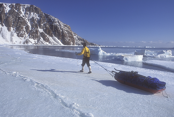 man pulling sled at edge of open water