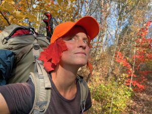 Katharina Kneip standing in colourful woodland with red maple leafs tucked into her hat