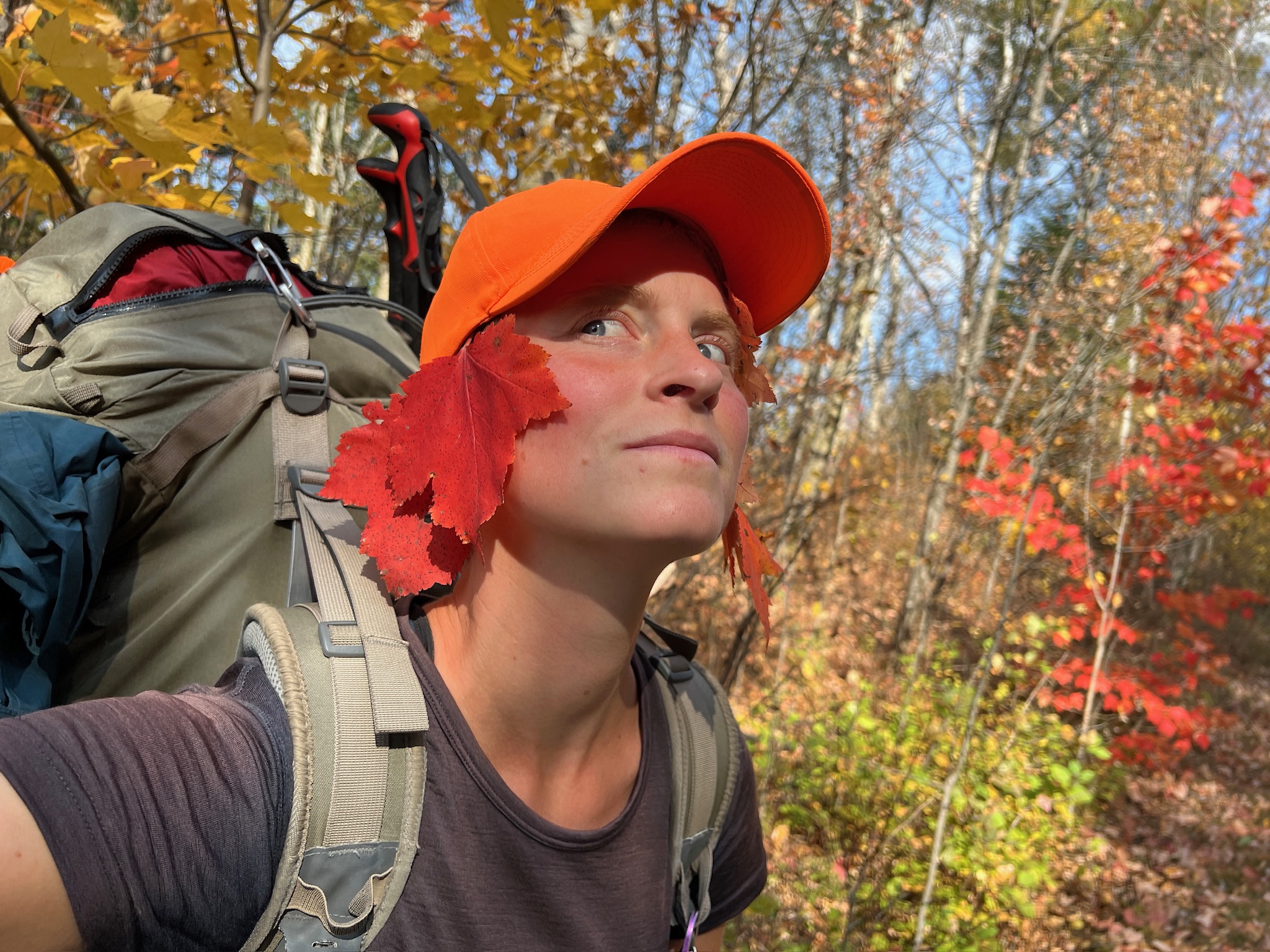 Katharina Kneip standing in colourful woodland with red maple leafs tucked into her hat