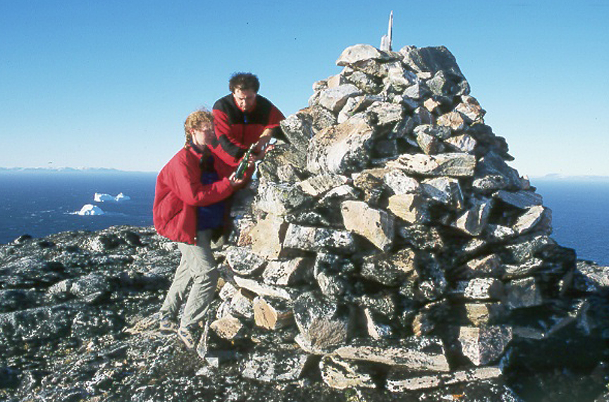 two people in red inspect a big cairn